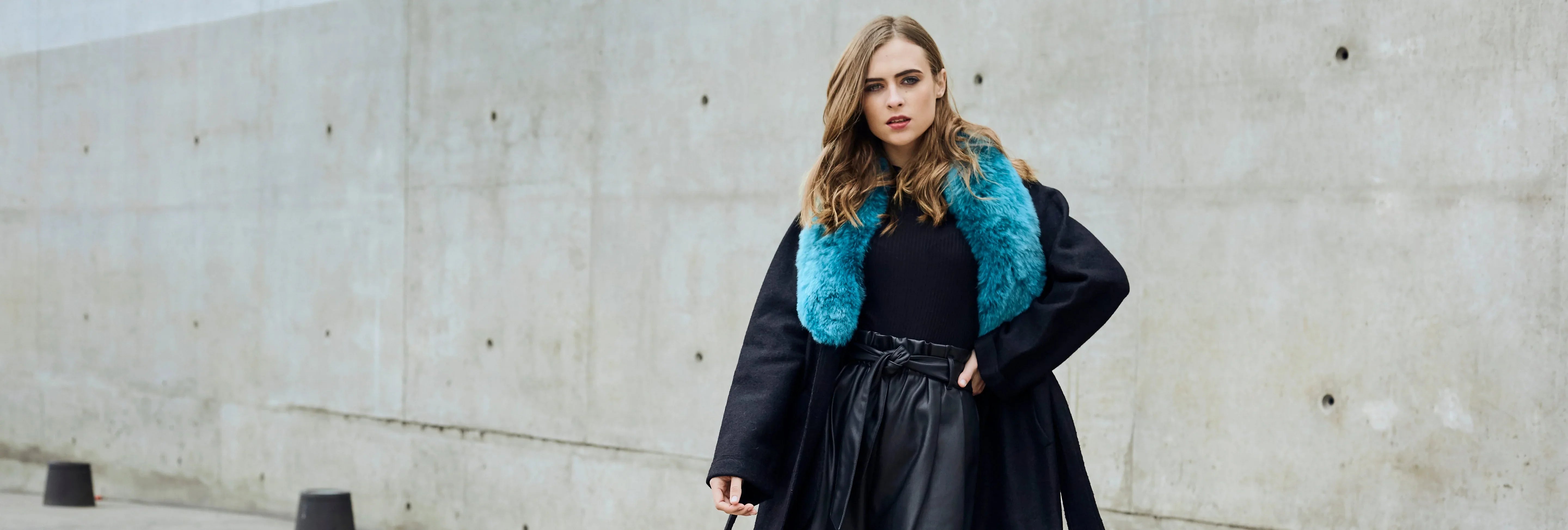 Woman in black overcoat with bright blue fur collar by NORGÄTE, luxury knitwear brand