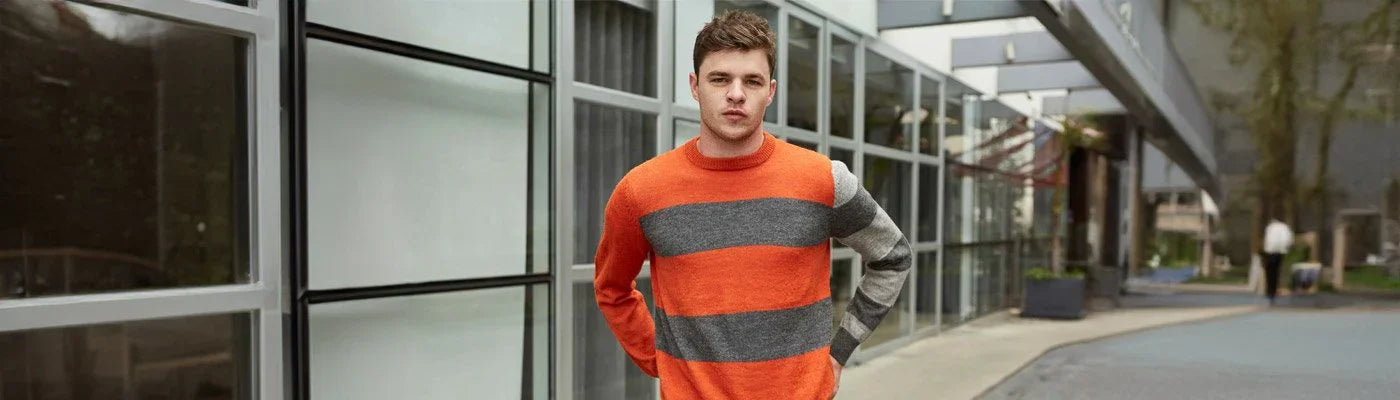 Man wearing orange and gray striped luxury knit sweater outside modern building, Norgäte